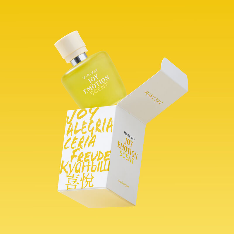 Mary Kay Joy Emotion Scent Eau de parfum yellow bottle emerging from product box on yellow background. 