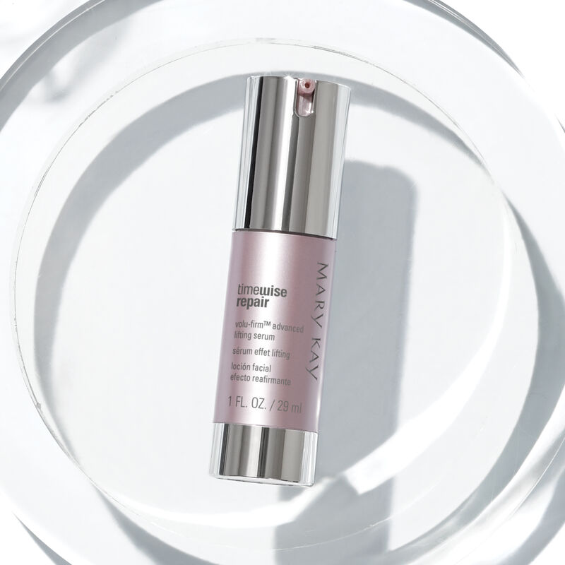 A bottle of Mary Kay TimeWise Repair Volu-Firm Advanced Lifting Serum laying on a clear platform with clear scientific accessories.
