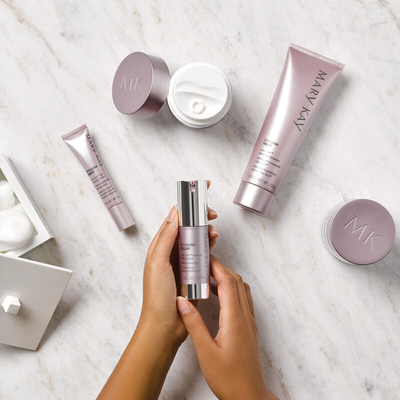 Hands holding a bottle Mary Kay TimeWise Repair Volu-Firm Advanced Lifting Serum over a marble table holding the TimeWise Repair Volu-Firm Set.