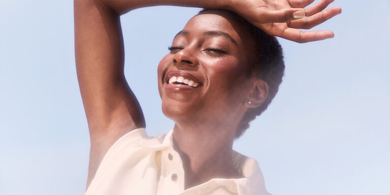 Modelo sonriendo bajo un cielo azul y el sol.