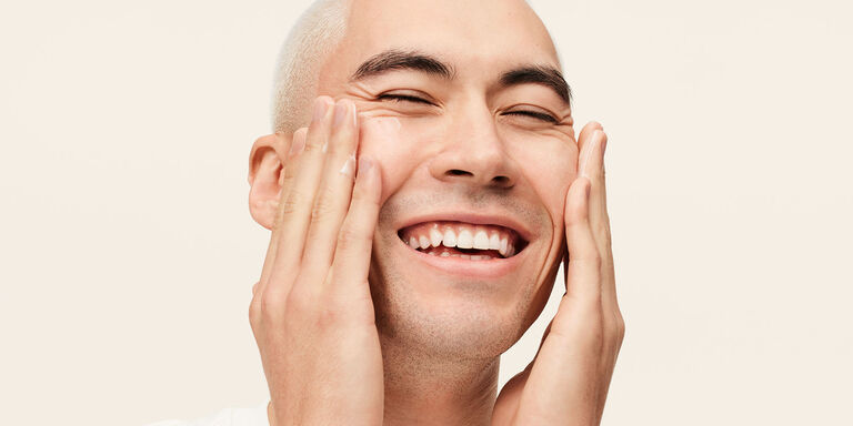 Modelo masculino sonriendo mientras aplica la Hidratante Avanzada MKMen&reg; en el rostro