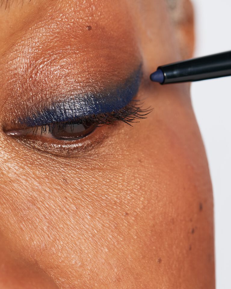 Close-up of a model applying blue eyeliner to her top lid
