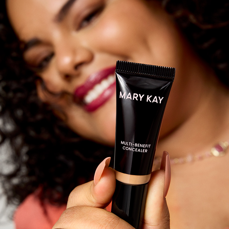 Mujer sonriendo y mostrando el Corrector Multibeneficios Mary Kay&reg; a c&aacute;mara.