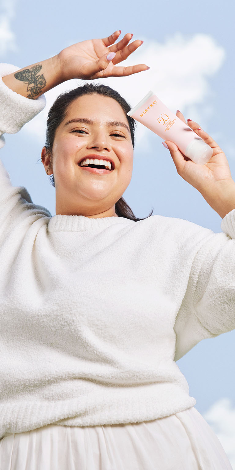 Modelo sosteniendo el Protector Solar FPS 50 Mary Kay bajo un cielo azul.