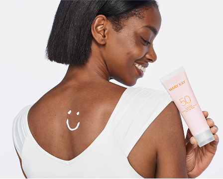 Modelo sosteniendo un envase de Protector Solar FPS 50 Mary Kay, con una cara sonriente dibujada con protector solar en la parte superior de la espalda.