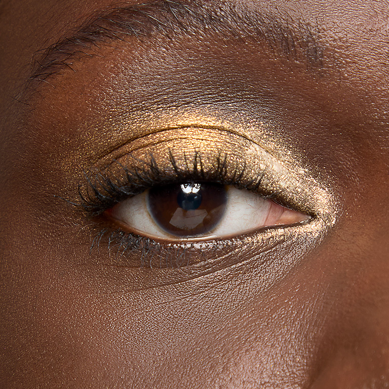 Mujer con tono de piel oscuro luciendo un look de sombras doradas.