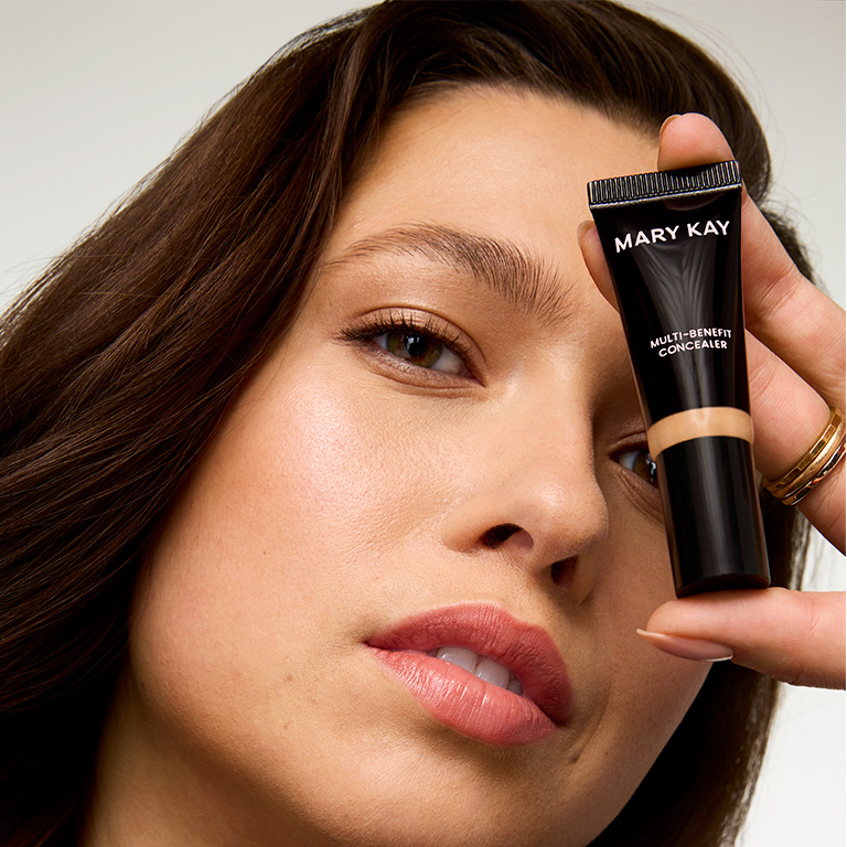 Mujer sosteniendo el Corrector Multibeneficios Mary Kay&reg; junto al rostro.