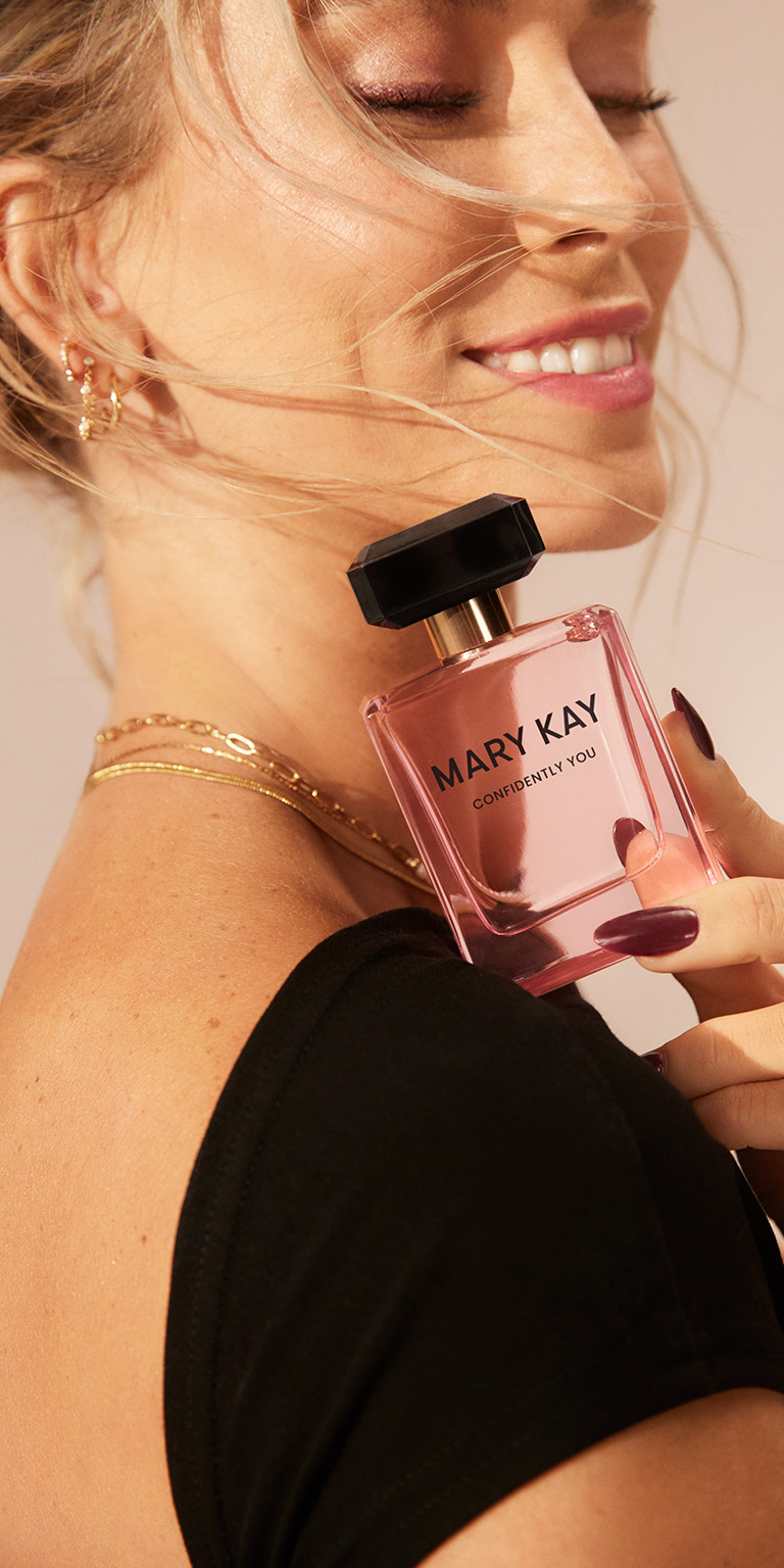 Mujer sosteniendo un frasco de Mary Kay Confidently You Eau de Parfum cerca del hombro, con un estilo elegante.