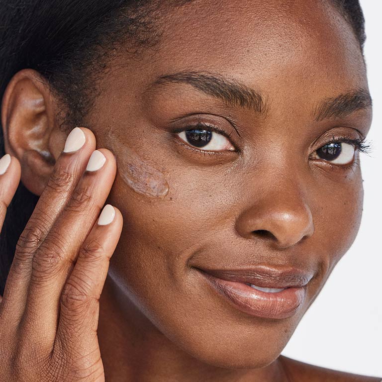 Mujer con tono de piel oscuro aplicando Gel Reparador para despu&eacute;s del Sol Mary Kay en la mejilla.