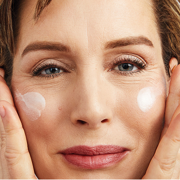 Mujer sonriendo a c&aacute;mara mientras aplica el S&eacute;rum Regenerador C+E TimeWise&reg; en ambas mejillas.
